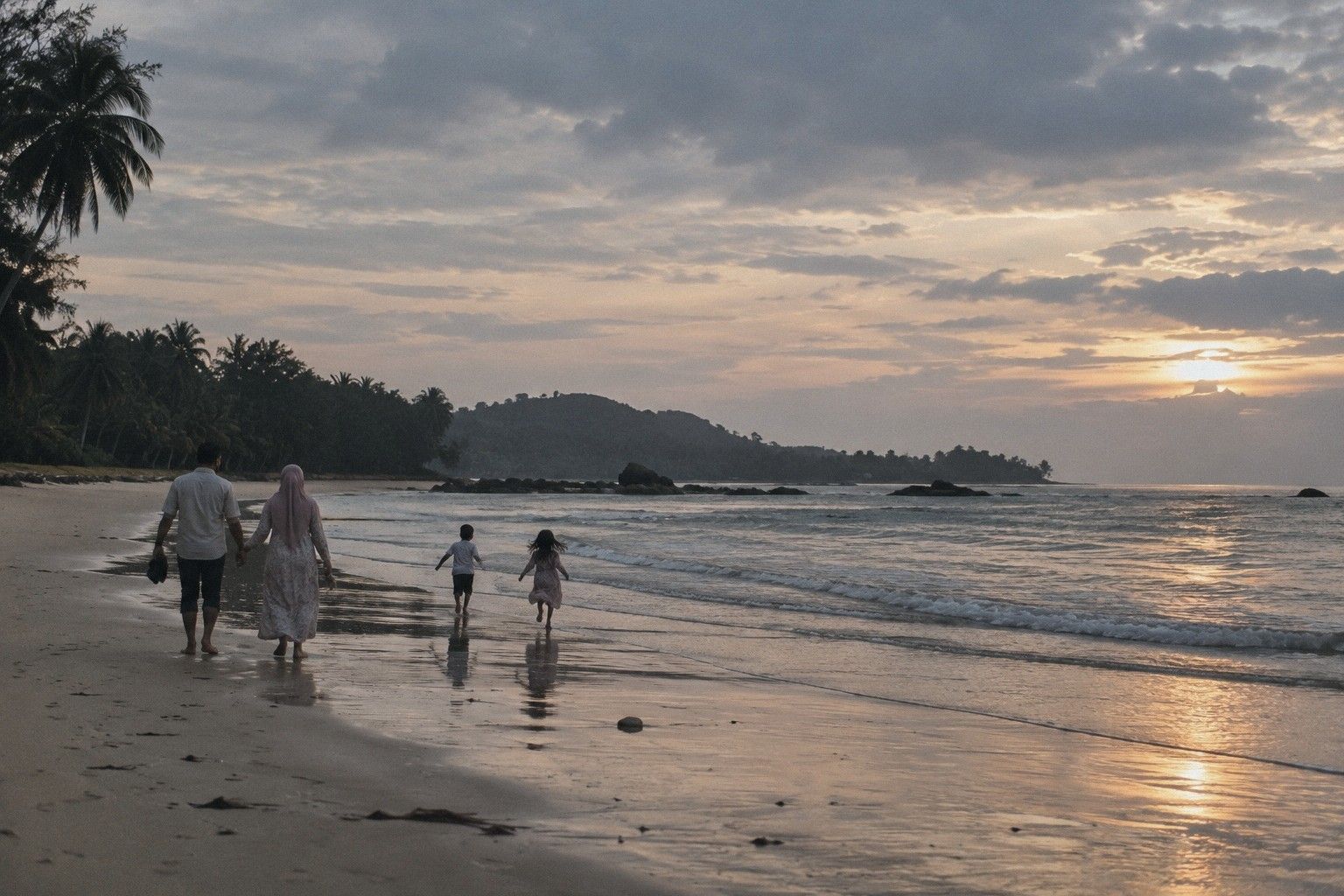 Sebuah keluarga berjalan di gigi air pantai waktu pagi, dilihat dari belakang, dua orang anak berlari di depan, langit kelabu jingga